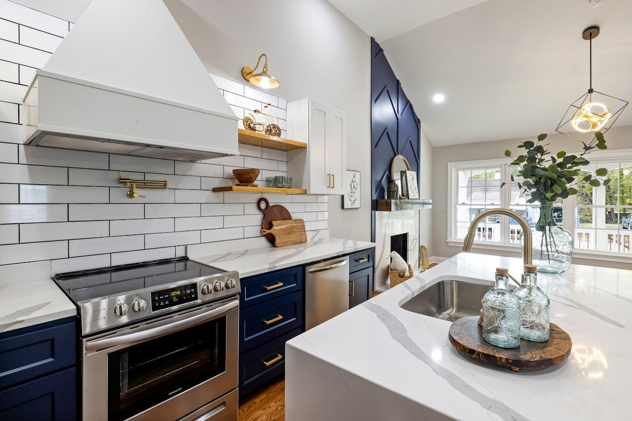A modern kitchen featuring marble countertops, a stainless steel stove, and elegant blue cabinets.