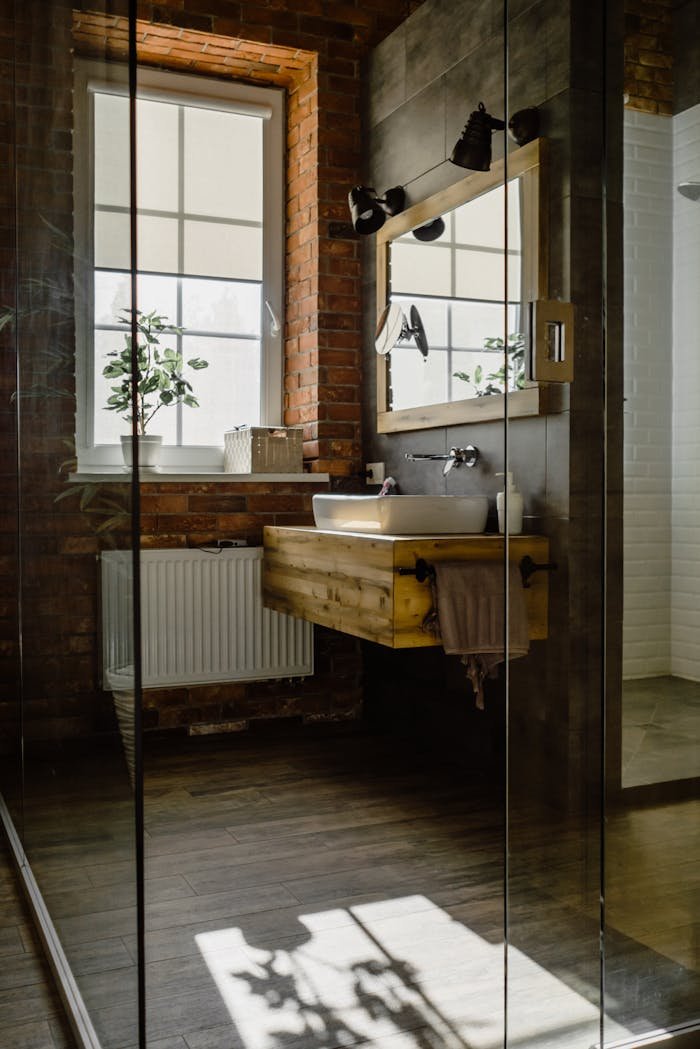 Modern bathroom with glass door, wooden sink, and natural brick wall.